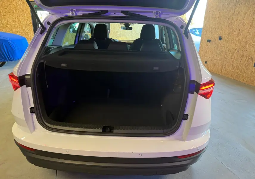 Vue arrière d’un Skoda Karoq blanc 2023 avec coffre ouvert, montrant l’espace de chargement et les feux arrière allumés.