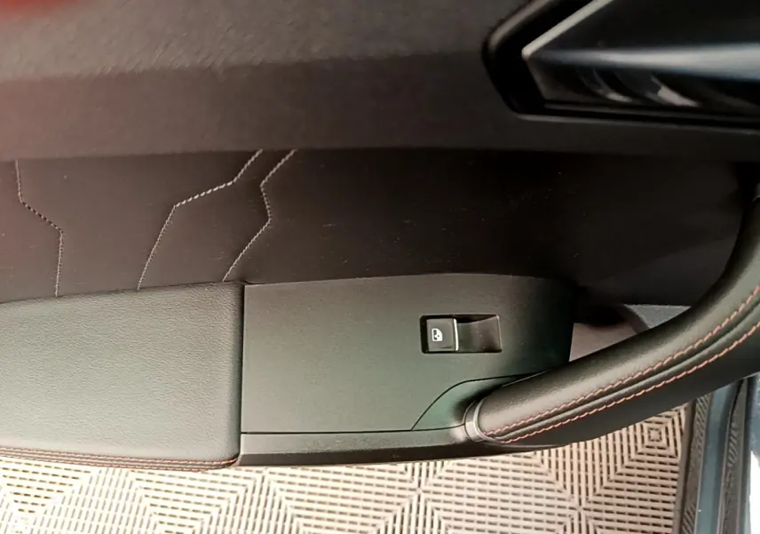 Détail de la porte côté conducteur d’une CUPRA Formentor gris foncé, avec bouton de verrouillage et surpiqûres rouges.