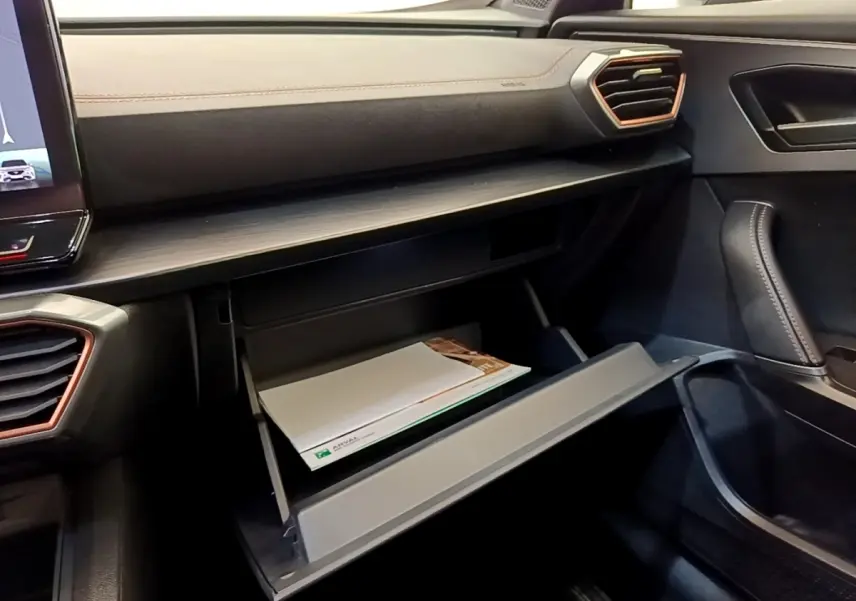 Intérieur côté passager de la CUPRA Formentor 2022, boîte à gants ouverte sous tableau de bord noir avec surpiqûres cuivre.