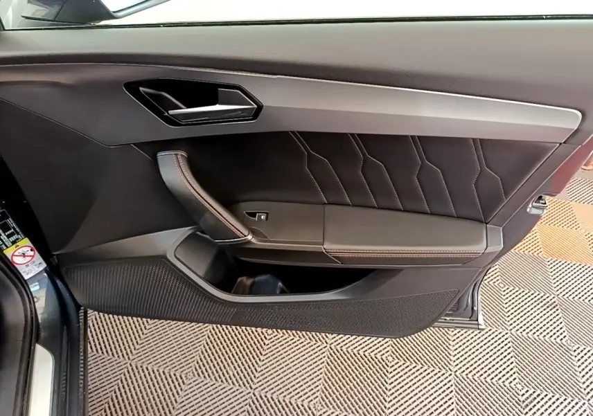 Vue intérieure côté gauche de la porte d’une CUPRA Formentor gris foncé avec garniture cuir et surpiqûres rouges.