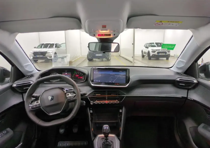Vue intérieure avant du Peugeot 208 gris clair 2025, avec tableau de bord carbone et écran tactile central 10 pouces.