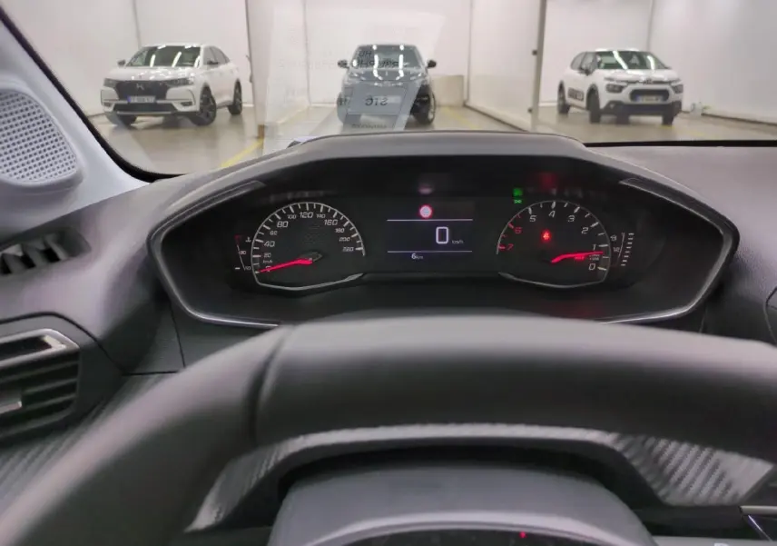 Vue depuis le poste de conduite du tableau de bord numérique de la Peugeot 208 gris clair, avec compteur et volant partiel visible.