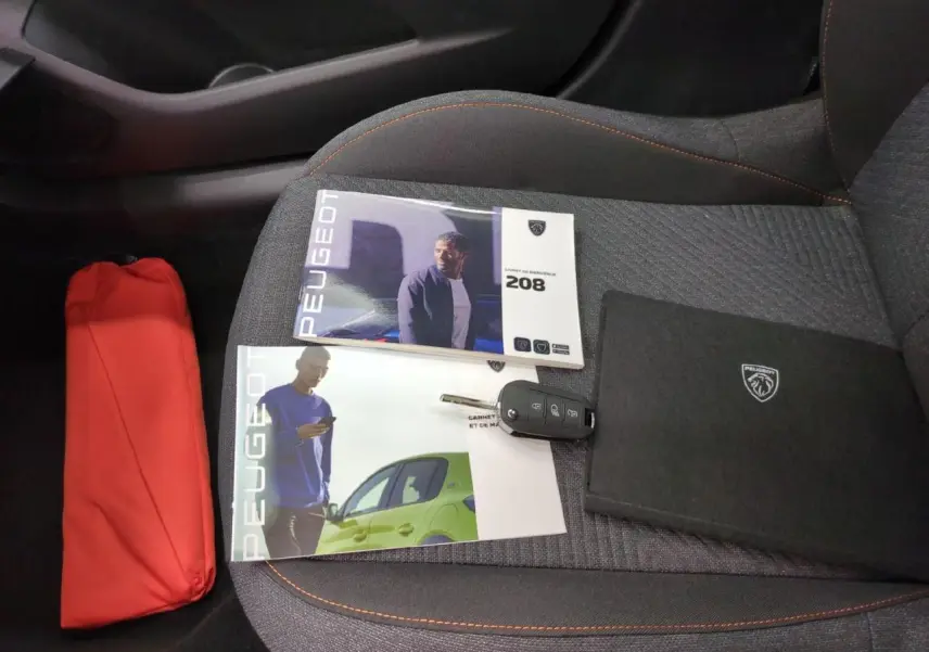 Vue intérieure du siège avant droit gris avec surpiqûres orange, clés et documents Peugeot 208 posés dessus.