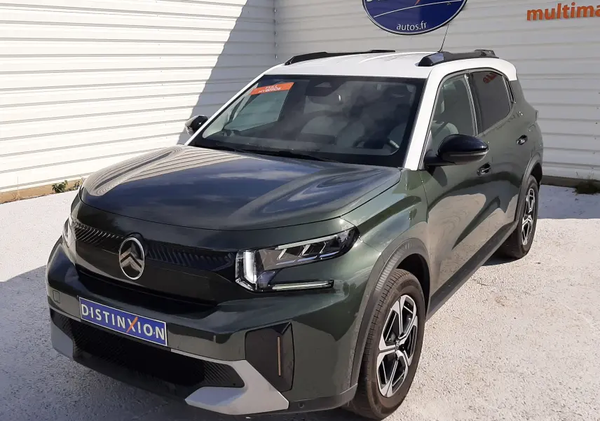 Vue 3/4 avant droite d'un Citroën C3 Aircross 2025 vert Montana avec toit blanc et jantes biton, stationné devant un mur blanc.