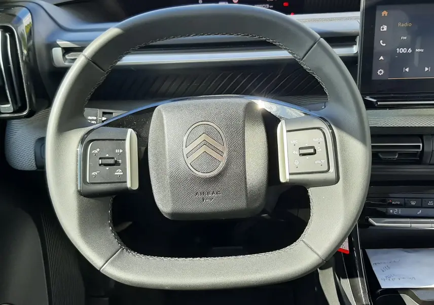 Vue rapprochée du volant noir de la Citroën C3 Aircross 2025, avec commandes intégrées et tableau de bord numérique en arrière-plan.