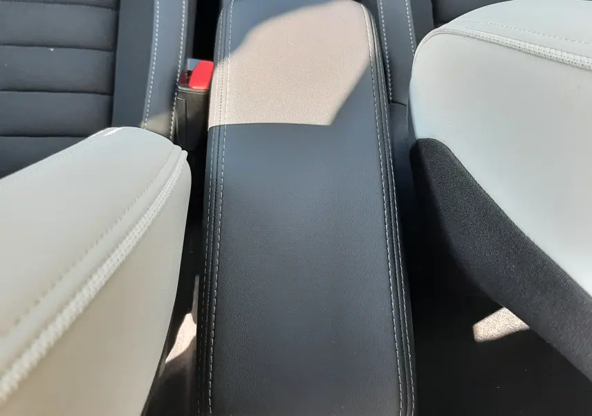 Vue rapprochée de l'accoudoir central noir entre les sièges avant en cuir clair du Citroën C3 Aircross 2025 hybride.