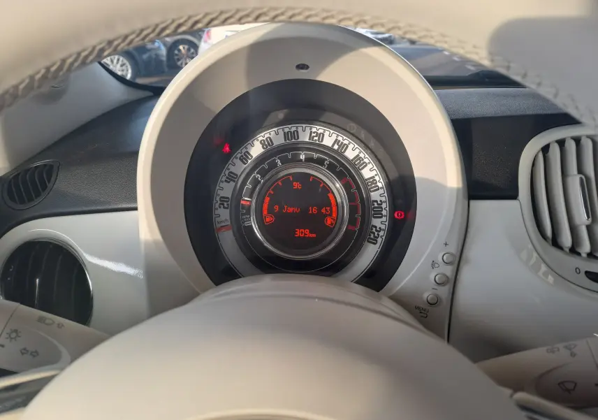 Vue rapprochée du tableau de bord blanc de la Fiat 500 2023, avec compteur circulaire et affichage digital rouge.