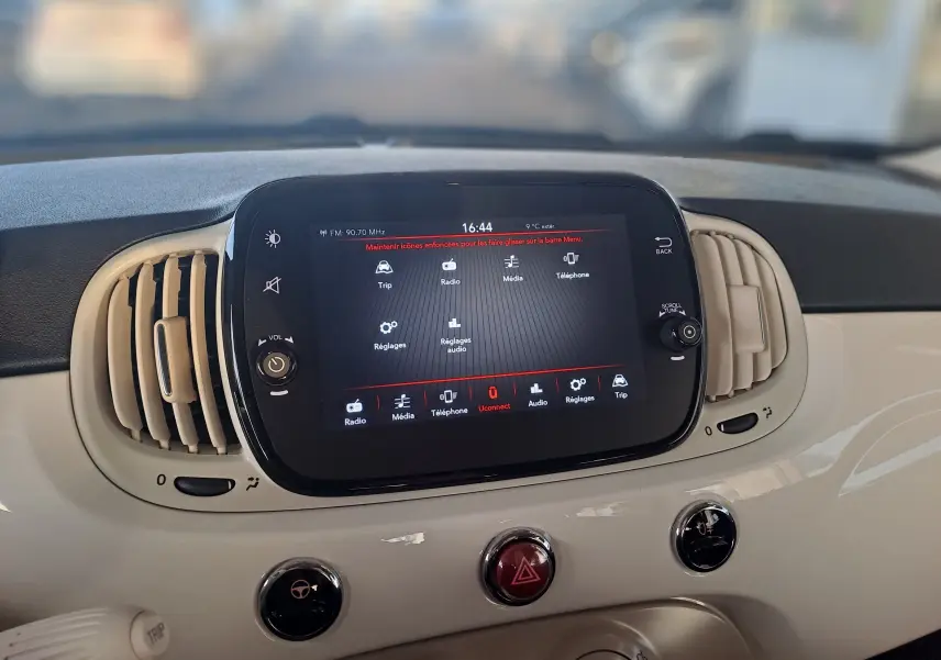 Écran tactile central allumé avec menu multimédia, entouré de la planche de bord beige d'une Fiat 500 blanche.