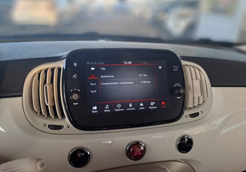 Écran tactile central affichant l'autonomie et les options multimédia dans l'habitacle blanc d'une Fiat 500 2023.