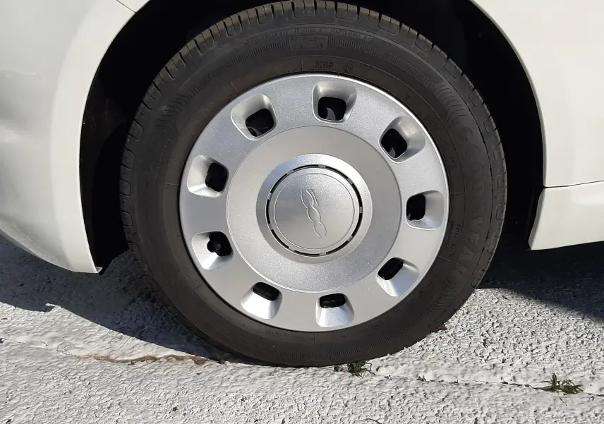 Gros plan sur la roue avant droite d'une FIAT 500 blanche 2023, mettant en valeur la jante avec logo central.