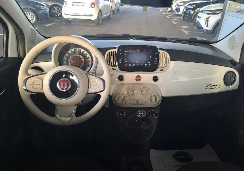 Intérieur de la Fiat 500 2023 en blanc, vue du poste de conduite avec volant beige et tableau de bord compact.