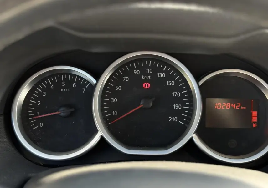 Gros plan sur le tableau de bord du Dacia Duster blanc, affichant le compteur et l'odomètre à 102842 km.