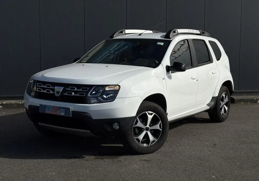 SUV Dacia Duster blanc glacier en 3/4 avant droit avec barres de toit alu et jantes diamantées noires.