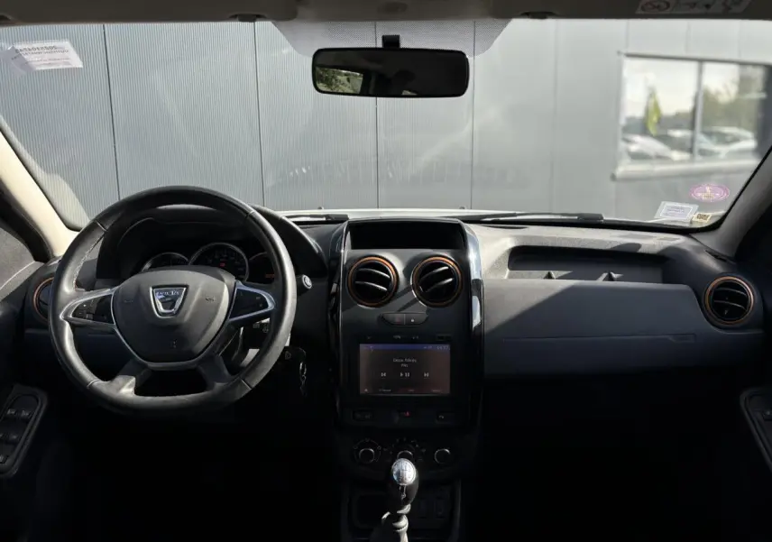 Vue frontale de l'intérieur du Dacia Duster blanc glacier 2017, volant cuir et écran GPS tactile au centre.