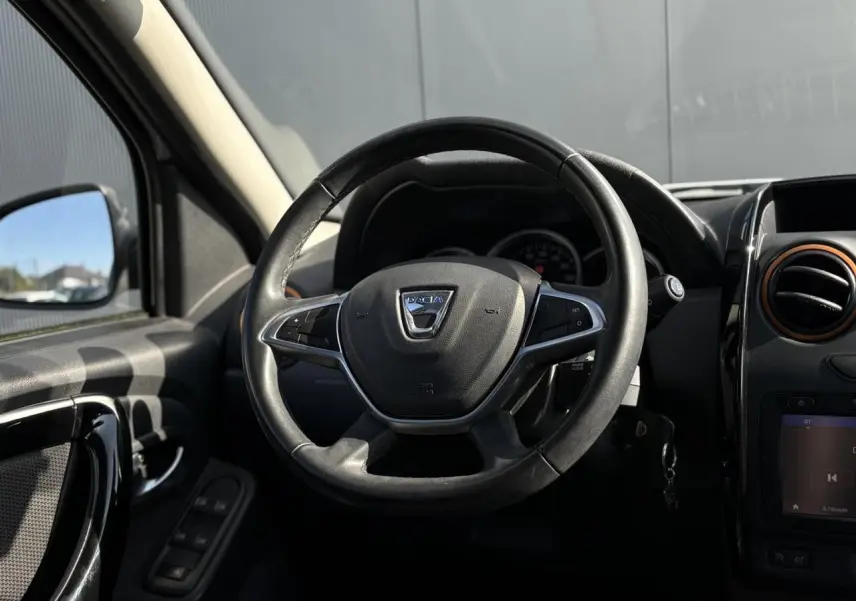 Vue rapprochée du volant en cuir noir du Dacia Duster TCE 125 Explorer, avec commandes multifonctions visibles.