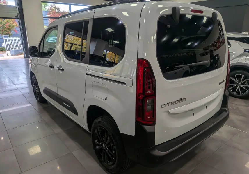 Vue 3/4 arrière droite du Citroën Berlingo blanc Glacier avec vitres teintées et jantes noires en showroom.