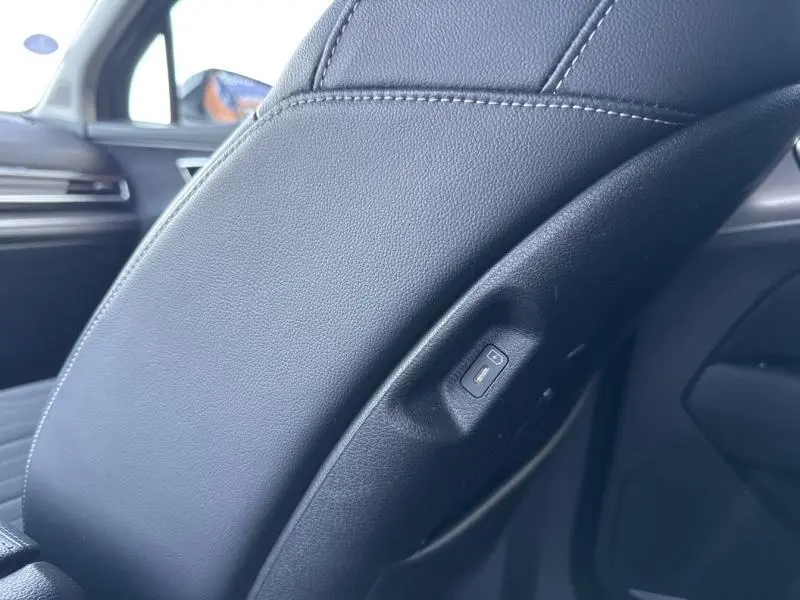 Détail du côté arrière du siège avant en cuir noir avec bouton de réglage dans l’habitacle du Kia Sportage noir Basalte.