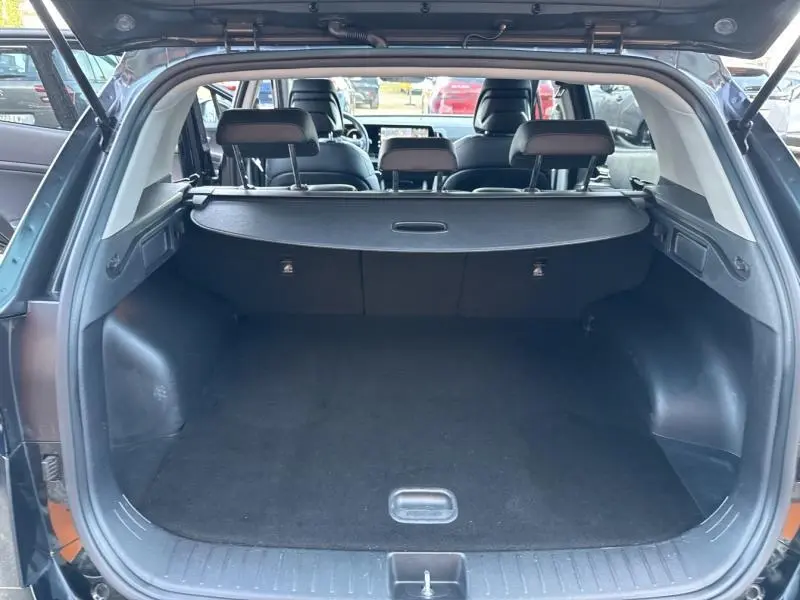Coffre ouvert vu de l'arrière du Kia Sportage noir Basalte métallisé, montrant l'espace de chargement et la banquette arrière.