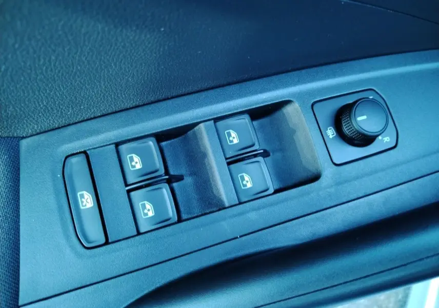 Gros plan sur les commandes des vitres électriques et réglage des rétroviseurs côté conducteur d'une Skoda Fabia blanche 2023.