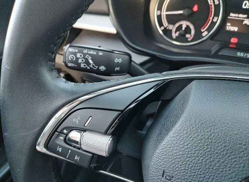 Gros plan sur la commande multifonction gauche du volant noir de la Skoda Fabia 2023, avec molette argentée et tableau de bord partiel.