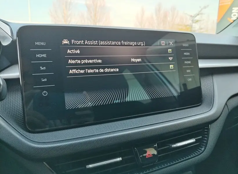 Écran tactile central du tableau de bord de la Skoda Fabia 2023 affichant les réglages de l'assistance freinage d'urgence Front Assist.