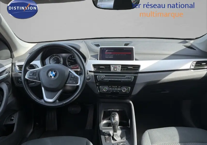 Intérieur de BMW X1 blanc 2022 vu de face, tableau de bord moderne avec écran central et volant multifonction.