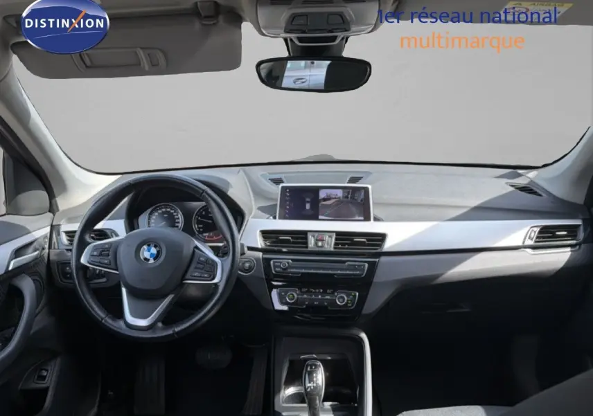Vue intérieure avant du BMW X1 blanc 2022, tableau de bord moderne avec écran central et volant multifonction.