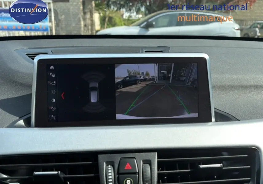 Écran central de BMW X1 blanc 2022 montrant la caméra de recul avec lignes de guidage en extérieur.