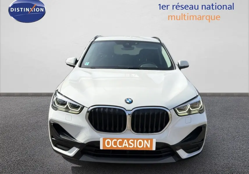 Vue frontale d'un BMW X1 blanc 2022 avec calandre noire et feux LED, sur fond neutre avec plaque "OCCASION".