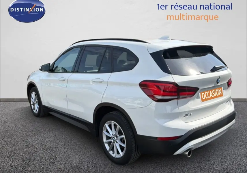 BMW X1 blanc vue 3/4 arrière côté gauche, avec feux arrière rouges et jantes alliage argentées.