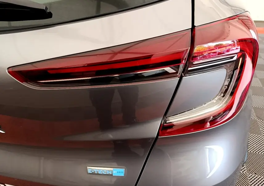 Gros plan sur le feu arrière droit et le logo E-Tech hybride d’un Renault Captur gris foncé 2022.