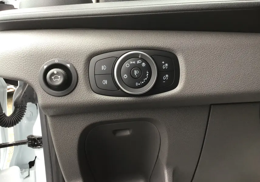 Détail du tableau de bord côté gauche du Ford Transit Fourgon blanc 2023 avec commandes d'éclairage et réglage des rétroviseurs.