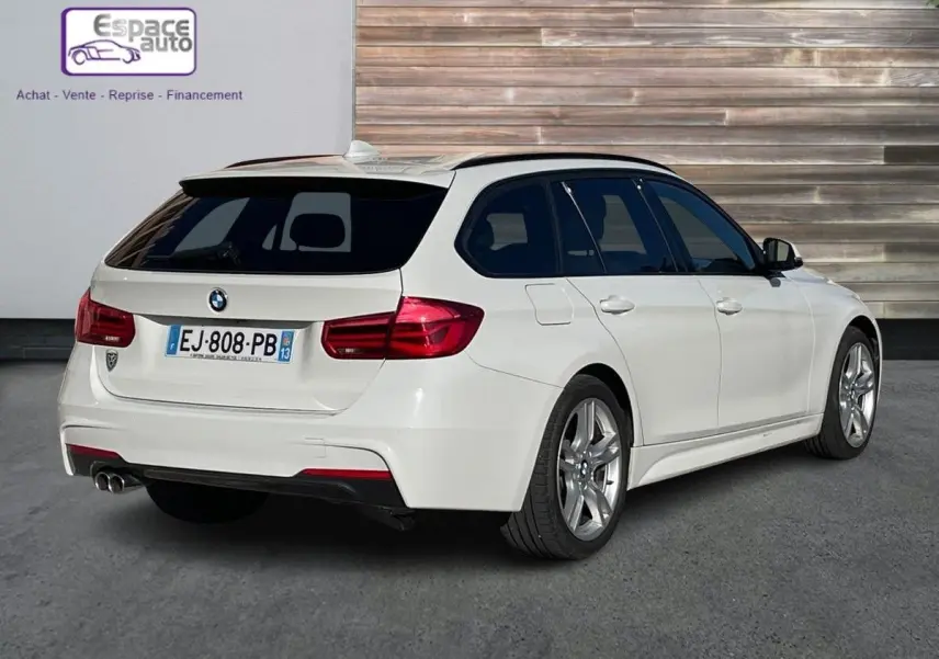 BMW Série 3 Touring F31 blanc vue 3/4 arrière droit avec double sortie d'échappement et vitres teintées.