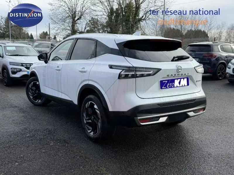 Vue 3/4 arrière droite d'un Nissan Qashqai blanc Hybrid e-POWER 205ch N-Connecta avec jantes noires sur parking.