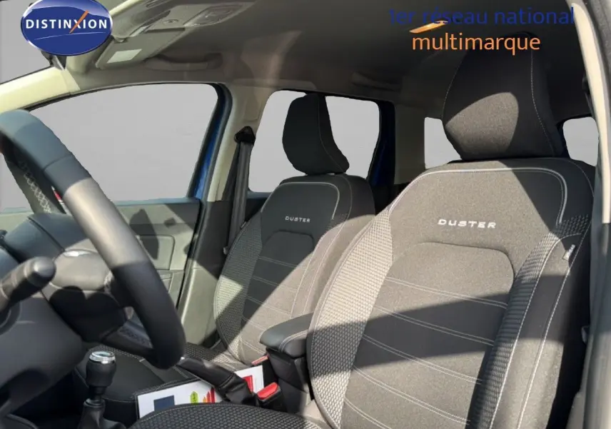 Vue intérieure côté conducteur du Dacia Duster 2022 bleu iron, mettant en valeur les sièges tissu gris avec logo Duster brodé.