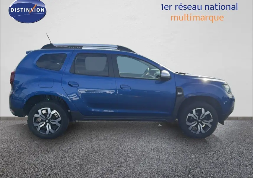 Profil droit d’un Dacia Duster 1.0 ECO-G 100 Prestige bleu Iron 2022 avec jantes bi-ton et barres de toit.