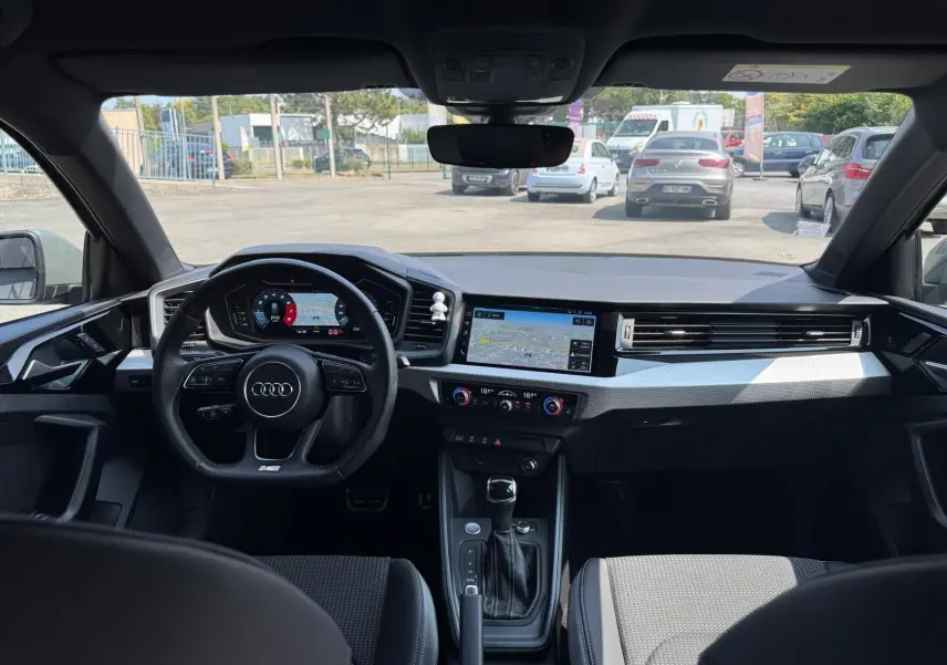 Vue intérieure avant de l'Audi A1 Sportback 2019, tableau de bord gris avec écran tactile et volant multifonction noir.