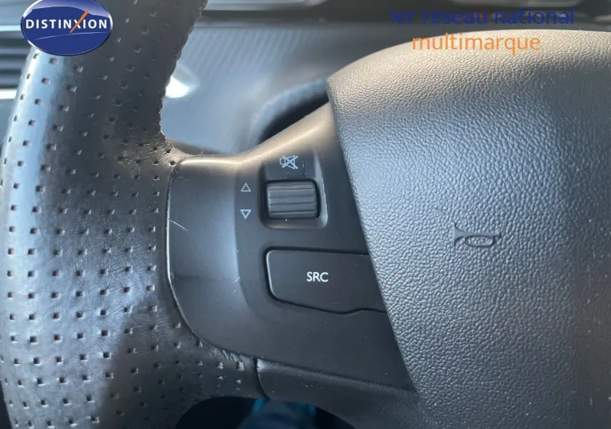 Gros plan sur le volant en cuir noir perforé du Peugeot 2008 gris platinium, avec commandes audio intégrées.