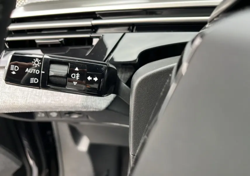 Gros plan sur la commande des feux et clignotants à gauche du volant dans l'habitacle du Peugeot 3008 Hybrid gris titane.