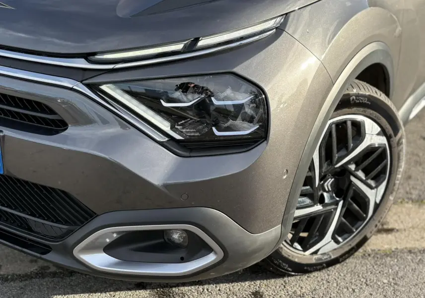 Gros plan sur l'avant droit gris Platinium de la Citroën C4 2024, mettant en valeur le phare LED et la jante alliage 18 pouces.