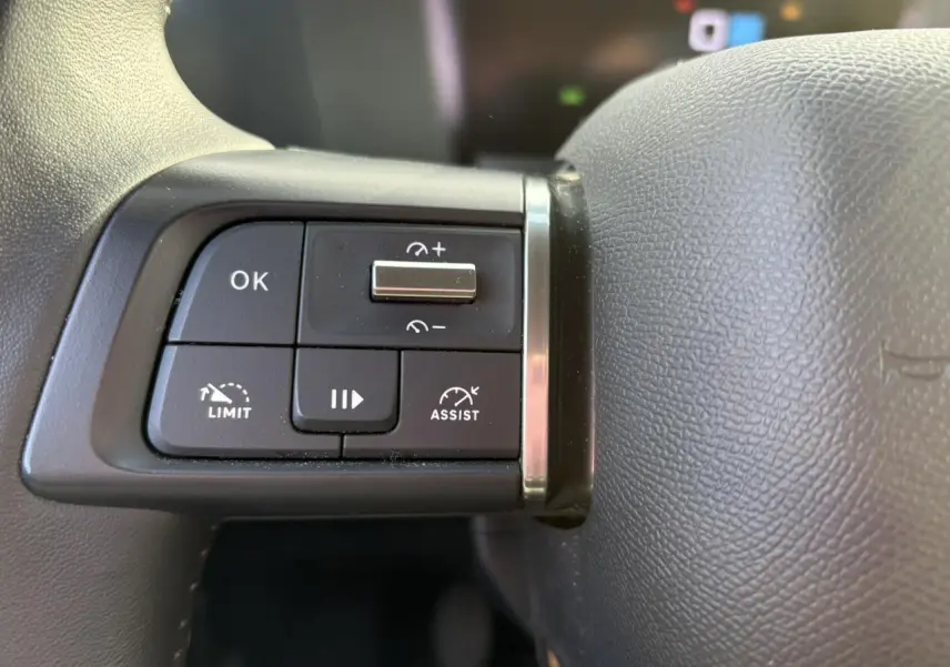 Gros plan sur les commandes noires au volant gris d'une Citroën C4 2024, avec boutons de régulateur et assistant de conduite.