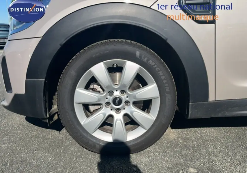 Gros plan sur la roue avant gauche d'une MINI Countryman grise avec jante alliage et logo MINI central visible.