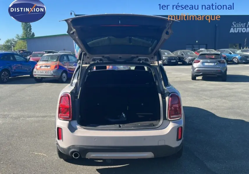 Vue arrière d'un MINI Countryman Cooper gris rooftop avec coffre ouvert sur un parking ensoleillé.