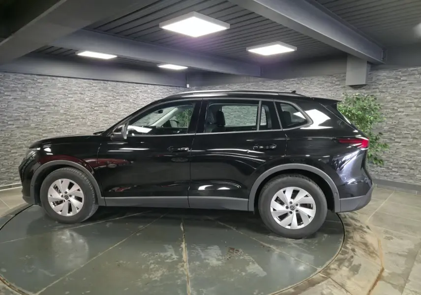 Vue de profil côté gauche d’un Volkswagen Tiguan noir 2025 avec jantes alliage 17 pouces dans un showroom.