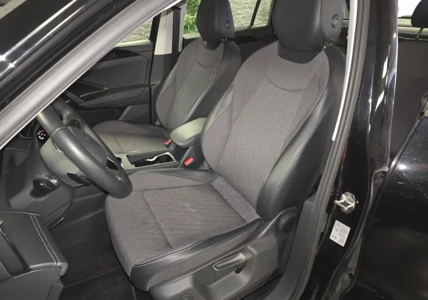 Vue intérieure côté conducteur du Volkswagen Tiguan noir 2025, sièges tissu et cuir gris avec accoudoir central.