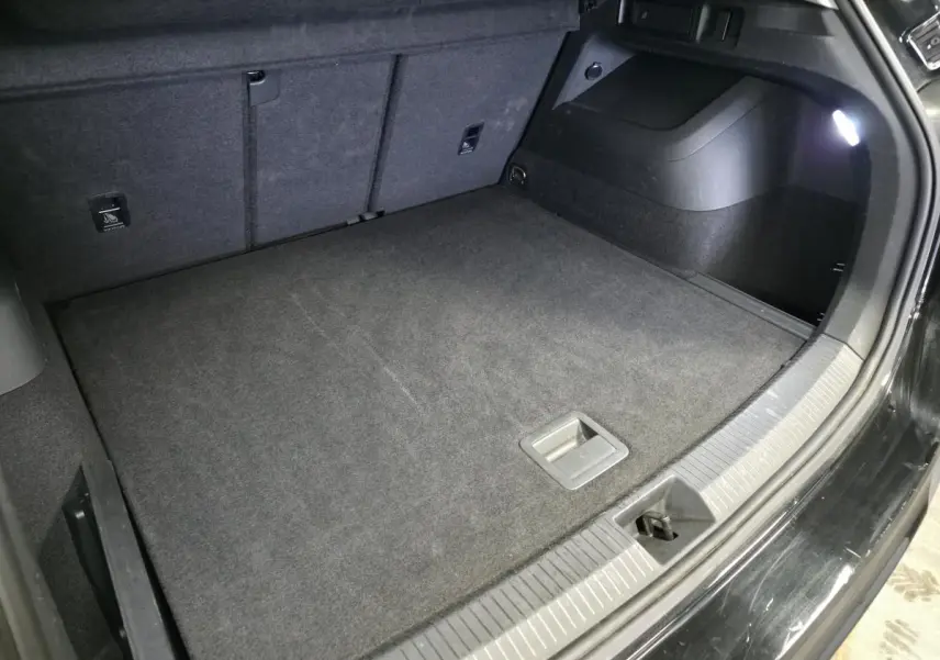 Coffre ouvert vu de côté droit, intérieur noir avec tapis de sol et éclairage LED, Volkswagen Tiguan noir 2025.