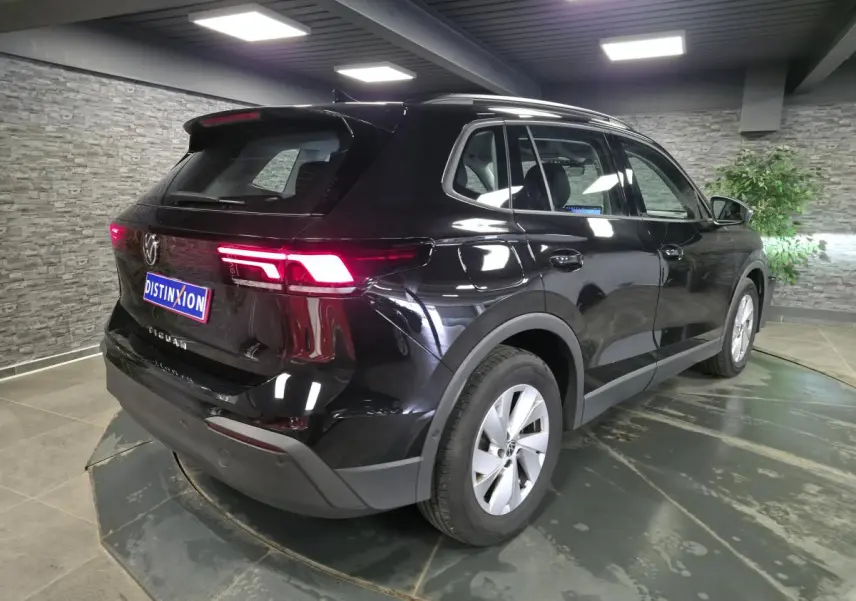 Volkswagen Tiguan noir métallisé vu en 3/4 arrière droit, avec feux arrière LED allumés et jantes alliage 17 pouces.