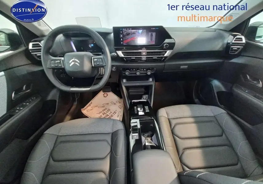 Intérieur avant de la Citroën C4 X 2023, vue centrée sur le tableau de bord et les sièges en cuir noir.