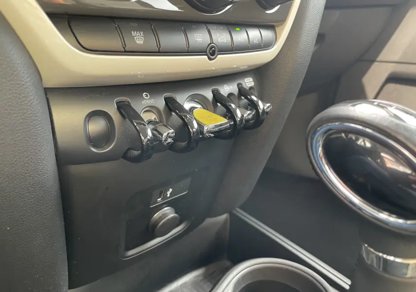 Gros plan sur la console centrale du MINI COUNTRYMAN F60 hybride, montrant les interrupteurs noirs et le bouton start/stop jaune.