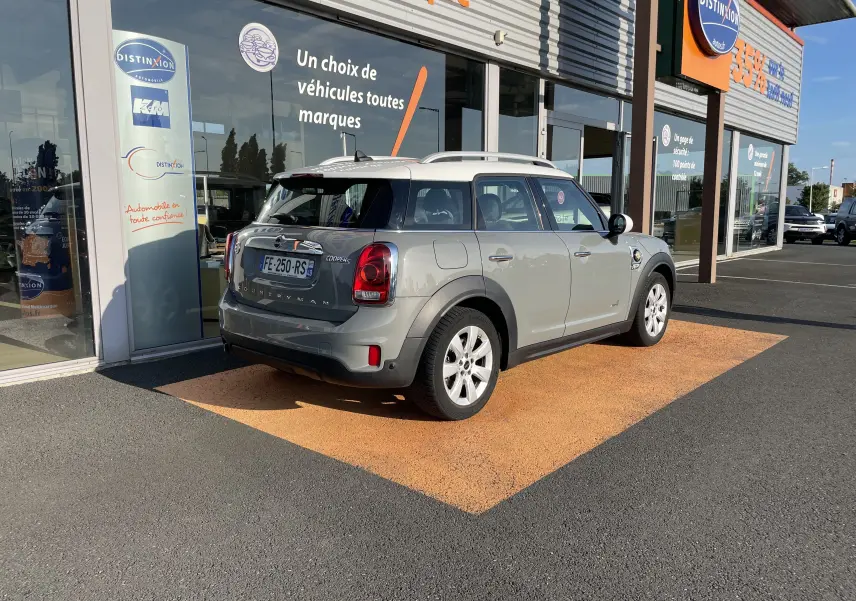 Vue 3/4 arrière droite d'une MINI COUNTRYMAN F60 hybride rechargeable Moonwalk Grey stationnée devant un concessionnaire.